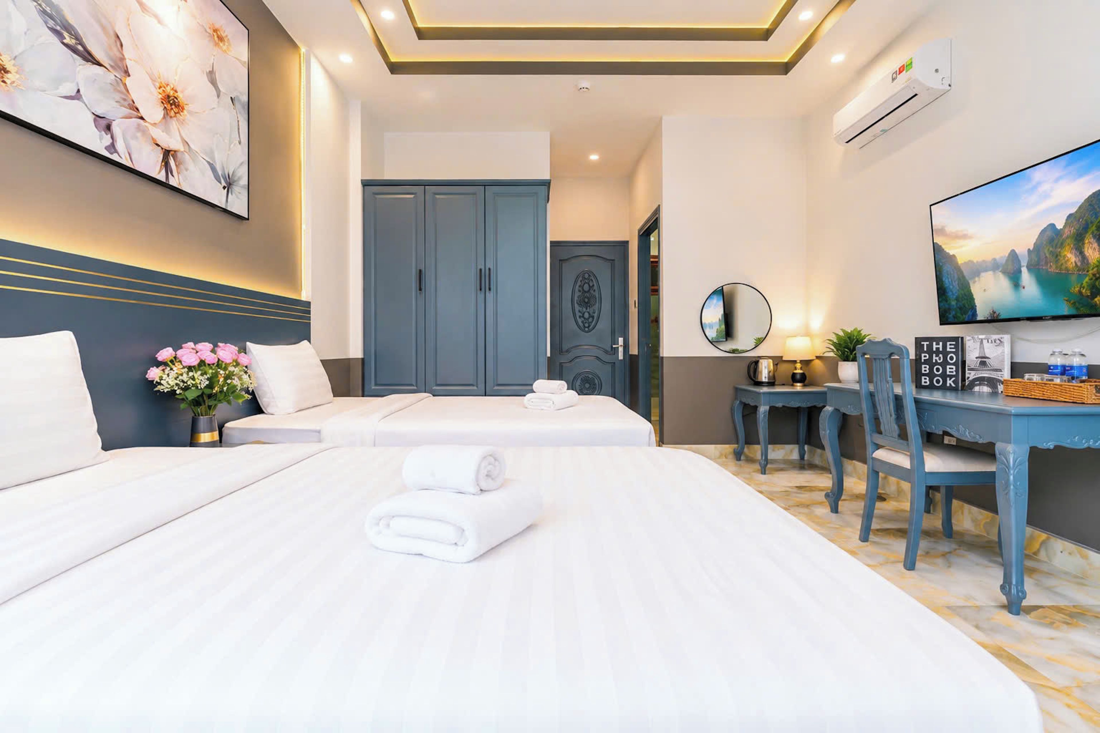 A hotel room with two beds, a desk with a chair, a TV, and a large window with a view.