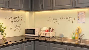 A kitchen with grey cabinets, a microwave, and a sink. There are decorative stickers on the wall and a plant on the counter.