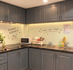 A kitchen with grey cabinets, a microwave, and a sink. There are decorative stickers on the wall and a plant on the counter. - Galang Hotel (Ho Chi Minh City)