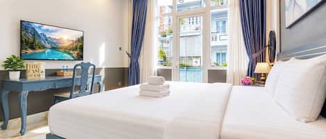 A hotel room with a bed, a desk, a chair, a TV, and a window with curtains.