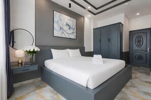 A modern bedroom with a large bed, a nightstand, a lamp, a vase with flowers, a wardrobe, and a door with an ornate design. - Galang Hotel (Ho Chi Minh City)