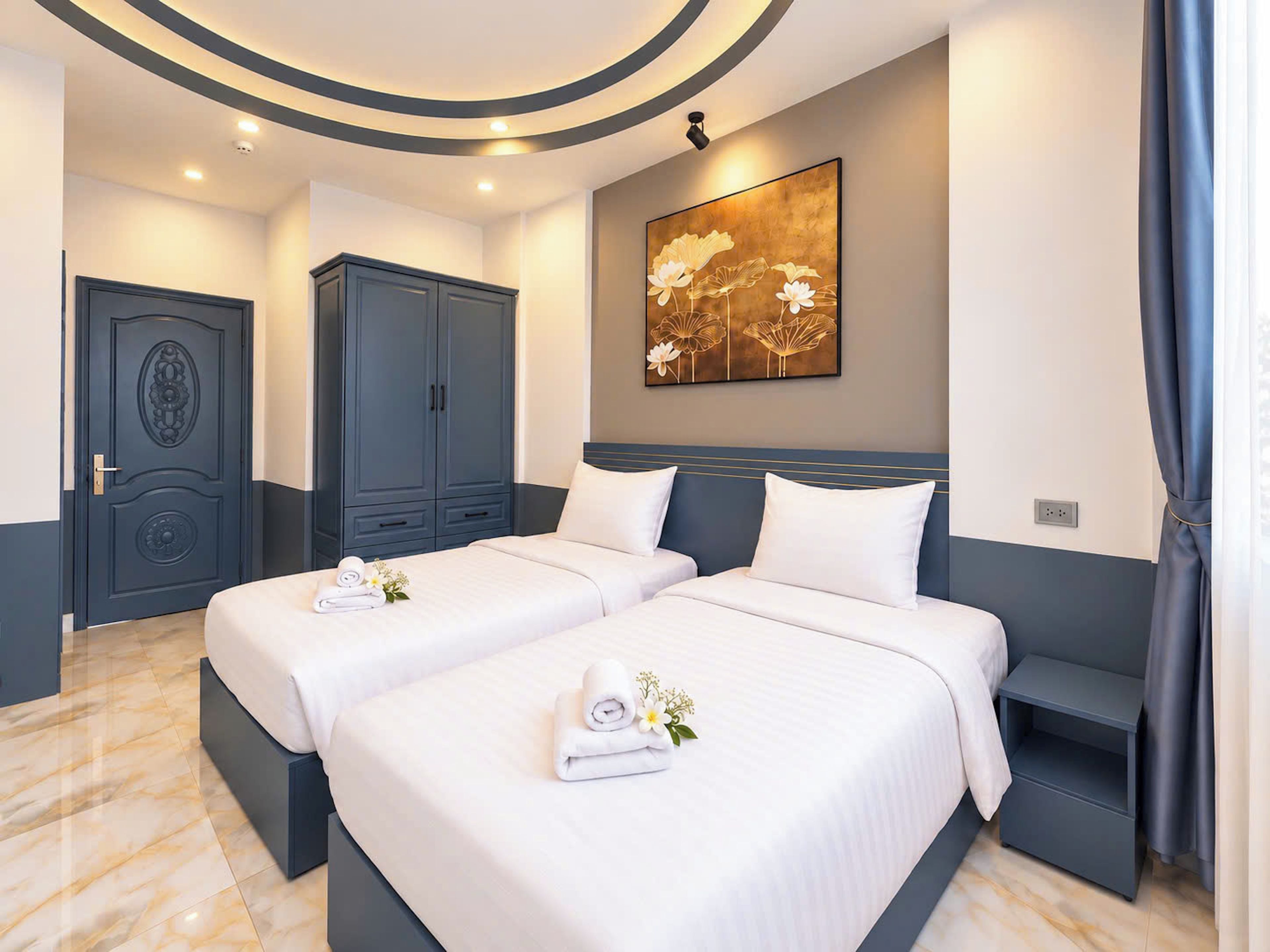 Habitación de hotel con dos camas, un armario grande, un cuadro en la pared y un baño visible a través de la puerta.