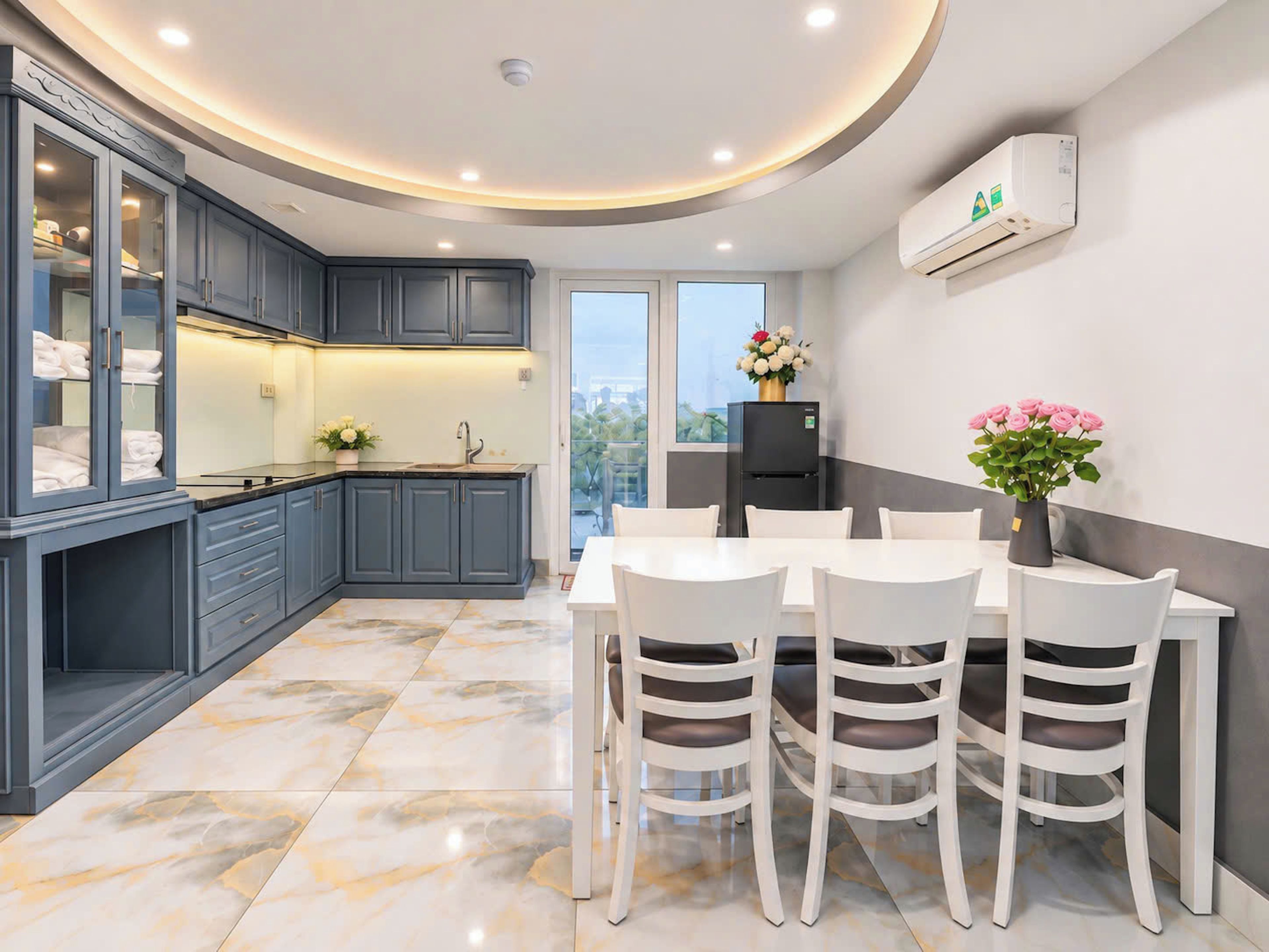 Una cocina moderna con armarios grises, un refrigerador negro y un comedor con sillas blancas y una mesa.