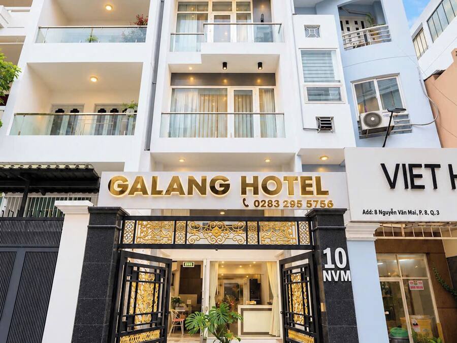 A hotel entrance with a modern design, featuring a large glass door, a signboard with the hotel's name, and a contact number.