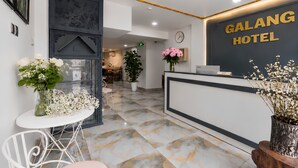 Zona de recepción de hotel con piso de mármol, mostrador de recepción y un reloj en la pared.
