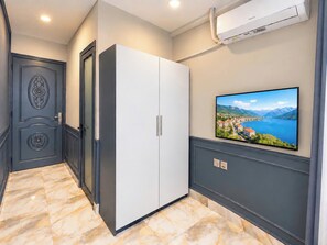 Un couloir avec une armoire blanche, un téléviseur fixé au mur diffusant un paysage, et un appareil de climatisation mural.