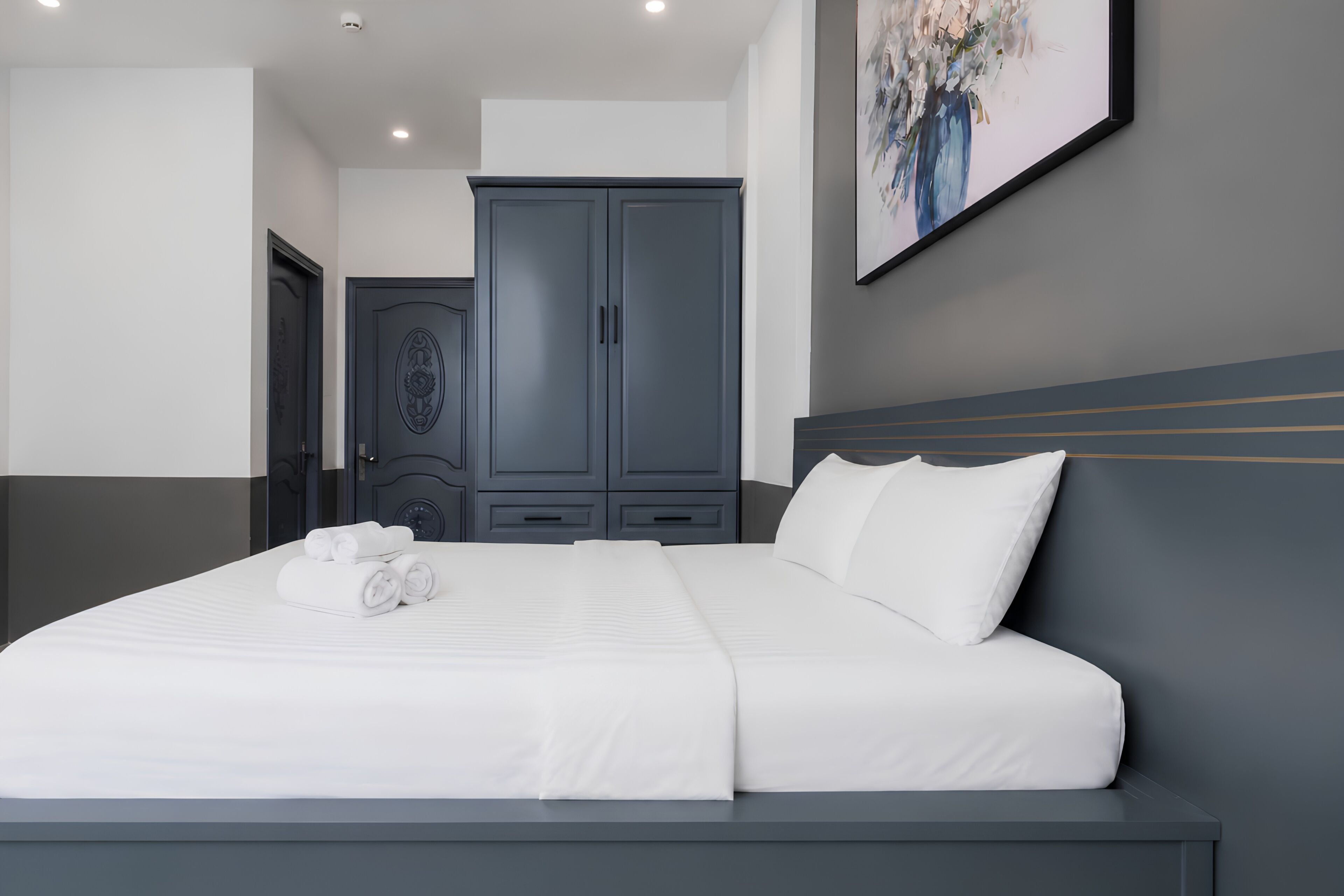 Ein modernes Hotelzimmer mit einem großen Bett, einem grauen Kleiderschrank und einem Bild an der Wand.