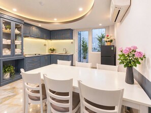 A modern kitchen with blue cabinets, a white dining table, and chairs. There is a refrigerator and a vase with flowers on the counter. - Galang Hotel (Ho Chi Minh City)