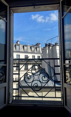 A view through a window with ornate metal railings, overlooking a building with multiple balconies and a clear blue sky. - Beautiful, bright, and quiet 2-room apartment in the Marais. 5th floor. (Paris)