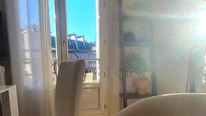 A room with two white armchairs, a wooden floor, a window with a view of buildings, and a radiator. - Lovely bright and quiet 2-room apartment, Marais. 5th floor. (Paris)