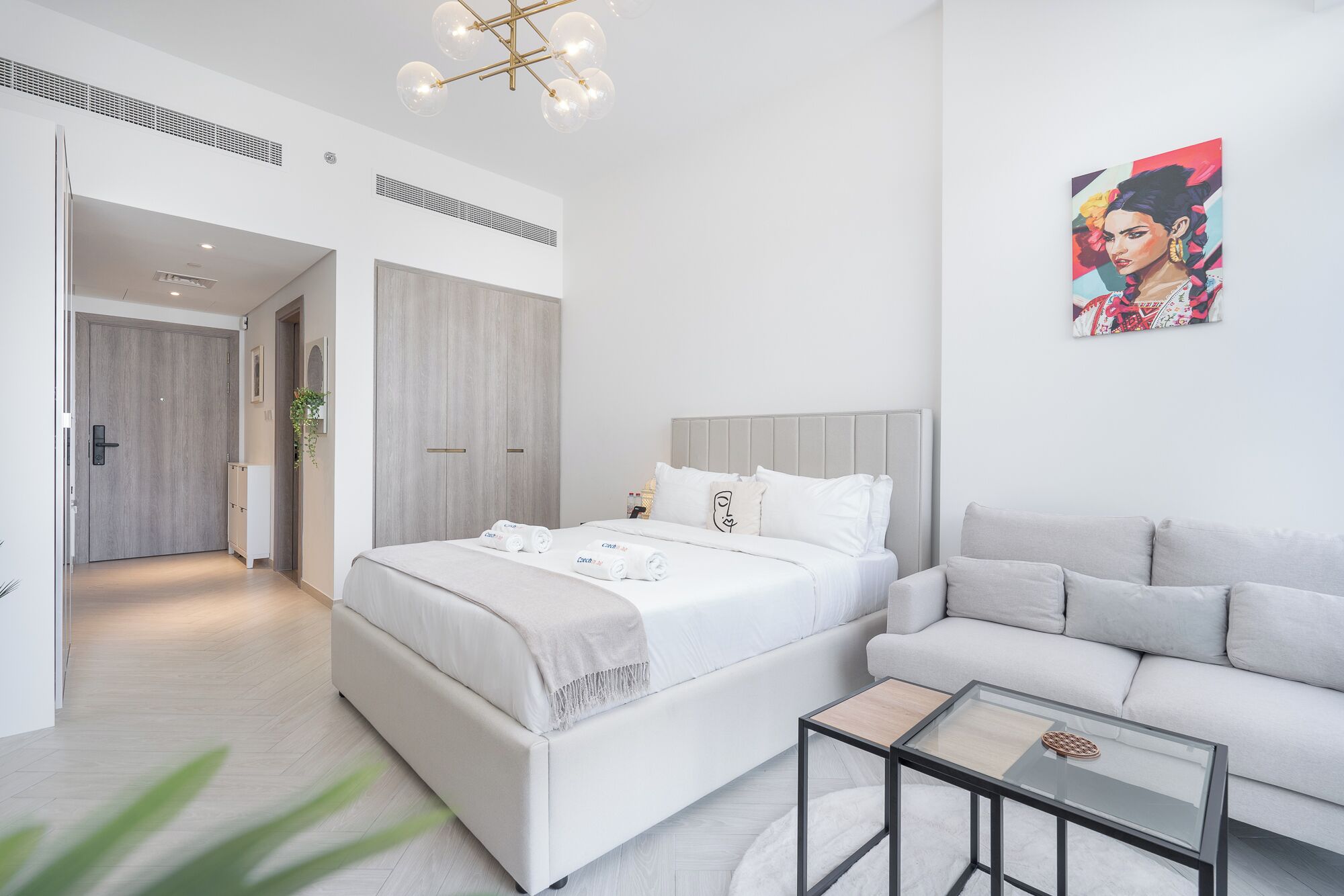 A modern hotel room with a large bed, a sofa, a glass coffee table, and a painting on the wall.