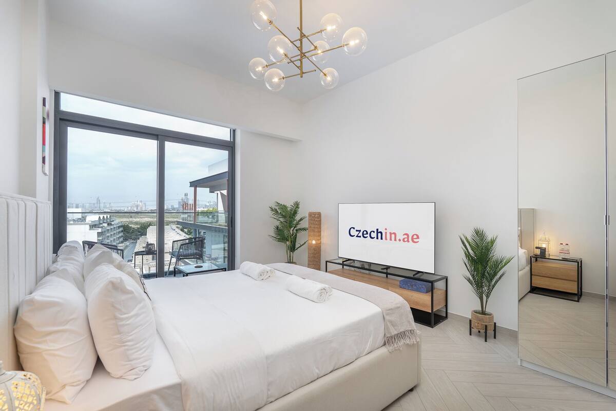 A modern bedroom with a large bed, a television, and a balcony with a city view.