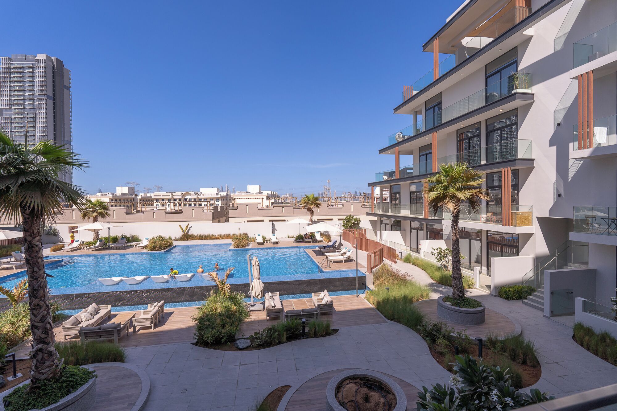 A rooftop swimming pool with lounge chairs and palm trees, surrounded by modern buildings.