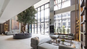 A spacious, modern living area with a large tree, comfortable seating, and large windows offering views of the city.