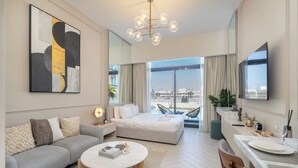A modern hotel room with a large bed, a sofa, a dining area, and a view of the city.