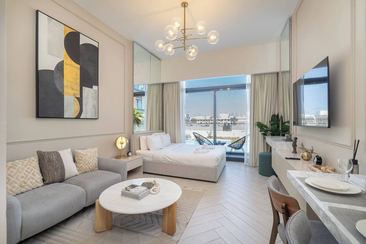 A modern hotel room with a large bed, a sofa, a dining area, and a view of the city.