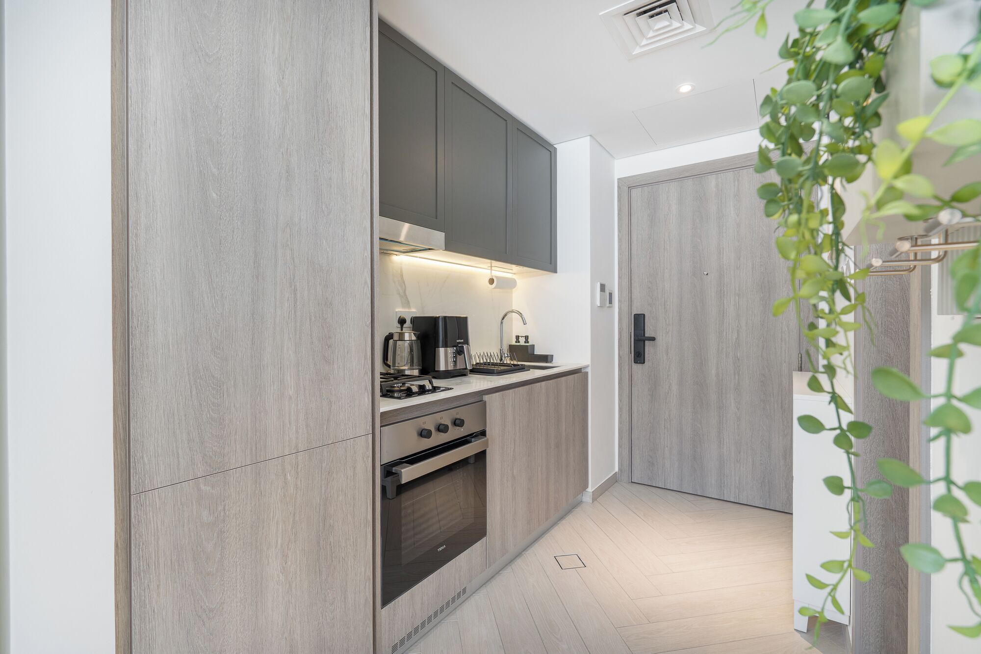 A modern kitchen with grey cabinetry, a built-in oven, and a coffee maker.