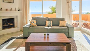 A living room with a sofa, a coffee table, a fireplace, and large windows with a view of the sea. - 3 bedroom penthouse apartment in Calahonda (Mijas Costa)