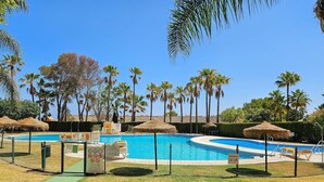A swimming pool surrounded by palm trees and a grassy area with a fence. - 3 bedroom penthouse apartment in Calahonda (Mijas Costa)