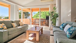 A spacious living area with a grey sofa, a wooden coffee table, and a grey armchair. There is a large sliding glass door leading to an outdoor patio with a table and chairs. - 3 bedroom penthouse apartment in Calahonda (Mijas Costa)