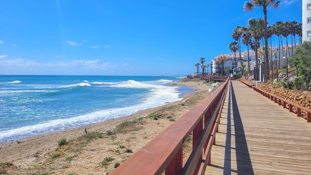 A wooden boardwalk along a beach with ocean views, palm trees, and buildings in the background. - 3 bedroom penthouse apartment in Calahonda (Mijas Costa)