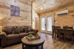 A cozy room with a wooden ceiling, a brown leather sofa, a wooden dining table with chairs, and a small round table with a plant and decorative items. - Oasis- A Creekside Resort, Pickleball , WIFI, Mountain Views, Starting at $79" (Cosby)