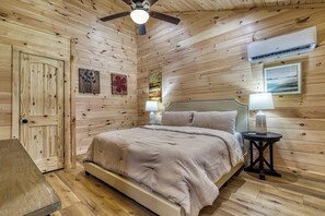 A wooden-paneled bedroom with a bed, bedside lamps, and a ceiling fan.
