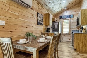 A wooden interior with a dining table set for four, a kitchen area, and a sign reading "KITCHEN".