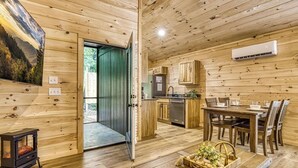 A wooden cabin interior with a dining area, kitchen, and a cozy fireplace.