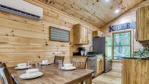 Ein Holzblockhaus-Interieur mit Esstisch für vier Personen, einer Küchenzeile mit Kühlschrank und einem Schild an der Wand.