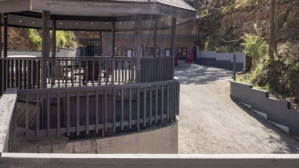 A gazebo with a tiled roof and a covered seating area, surrounded by a fenced outdoor space with trees and a dirt path. - Walk to Downtown, Parking, King Bed, Patios (Eureka Springs)