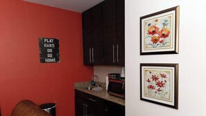 A compact kitchen with dark cabinets, a red accent wall, and a sink. - Walk to Downtown, Parking, King Bed, Patios (Eureka Springs)