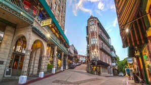 A historic building with a prominent arched entrance, a sign for the 'Basin Park Hotel,' and a street with a sidewalk and parked cars. - Walk to Downtown, Parking, King Bed, Patios (Eureka Springs)