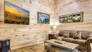 A cozy living room with wooden walls, a brown leather sofa, a coffee table, and a painting of a sunset. - Queens Quarters- Pickleball Court, Creek, WIFI, Mountain Views, Starting at $79" (Cosby)