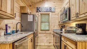 Une cuisine compacte dotée de meubles en bois, de plans de travail en granit, d’un réfrigérateur en acier inoxydable, d’un four à micro-ondes et d’une fenêtre avec des stores.