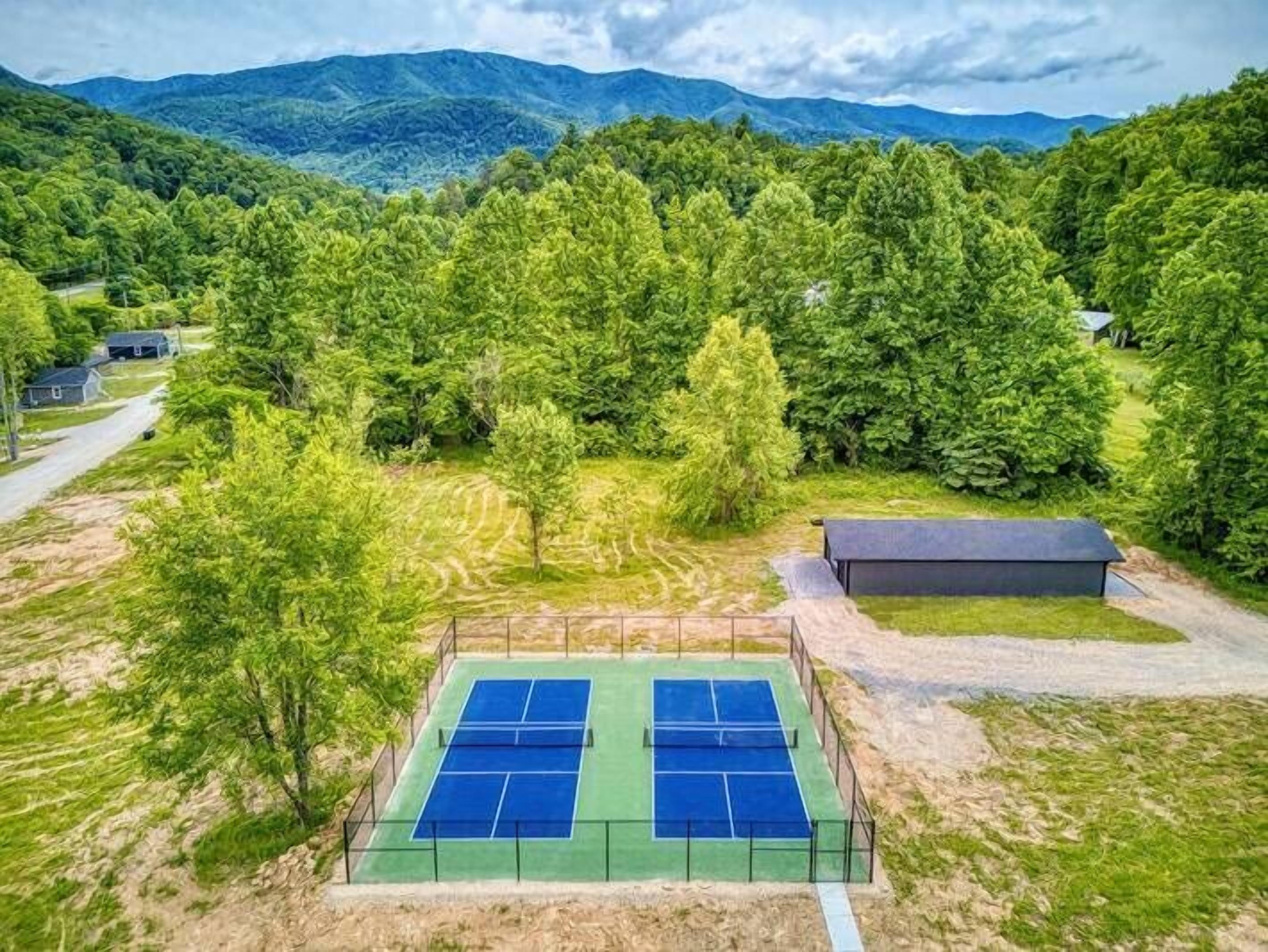 A tennis court surrounded by lush greenery and mountains in the background.