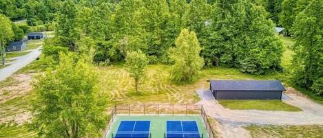 A tennis court surrounded by lush greenery and mountains in the background.
