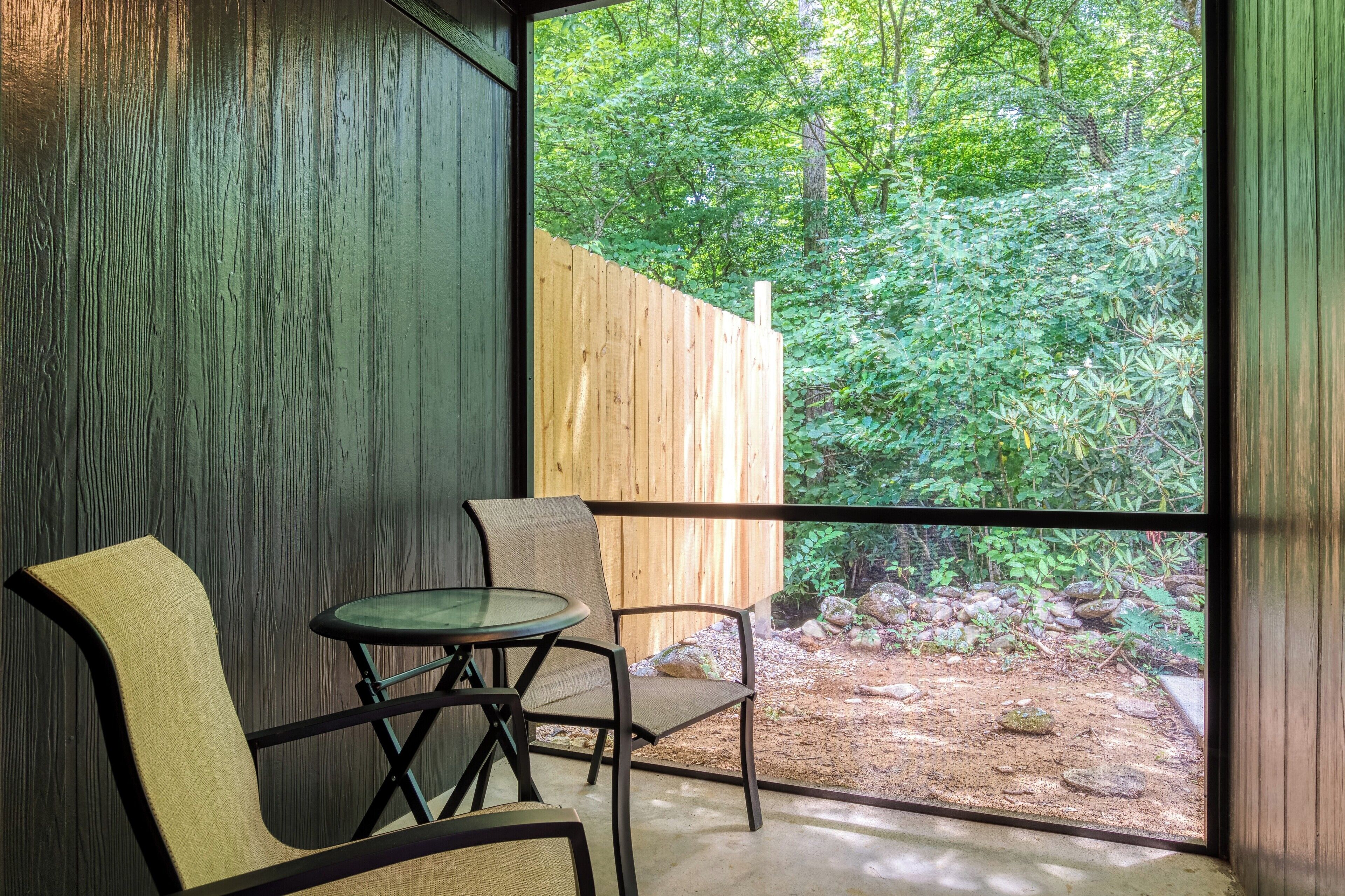 A room with a large window, a wooden wall, and a view of a forest.
