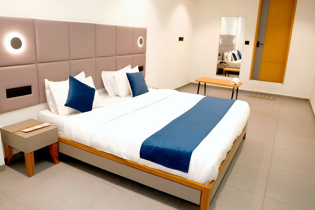 Ein modernes Hotelzimmer mit einem großen Bett, Nachttischen, einer Ablagefläche und einer Holzbank sowie einem Spiegel.