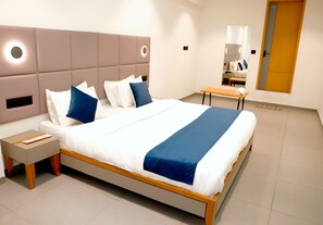 A modern hotel room with a large bed, bedside tables, a nightstand, a wooden bench, and a mirror. - Hotel Rio Orbit (Rajkot)