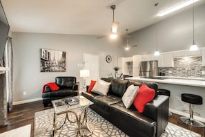 A modern living room with a black leather sofa, a glass coffee table, and a dining area with a white table and chairs.