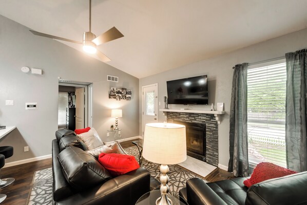 A modern living room with a fireplace, leather sofas, a television, and a ceiling fan.