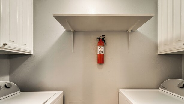 A laundry area with two white washing machines, a white shelf above, and a red fire extinguisher mounted on the wall. - I54-1 - Apt|Patio|11mi to Convention Ctr|Sleeps 2 (Irving)