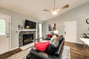 A living room with a fireplace, a black leather sofa, a television, and a ceiling fan.