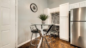 A kitchen with a glass-top table, two bar stools, a stainless steel refrigerator, and a potted plant. - I54-1 - Apt|Patio|11mi to Convention Ctr|Sleeps 2 (Irving)