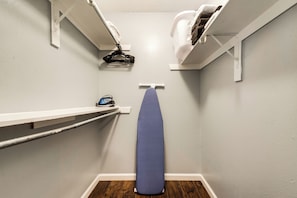 A laundry area with a hanging rack, ironing board, and a shelf with a small appliance.
