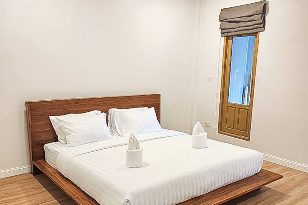 Un dormitorio con estructura de cama de madera, ropa de cama blanca y una ventana con un adorno marrón.