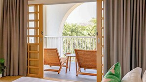 Una habitación con balcón, dos sillas de mimbre, una mesita y vistas a zonas verdes.