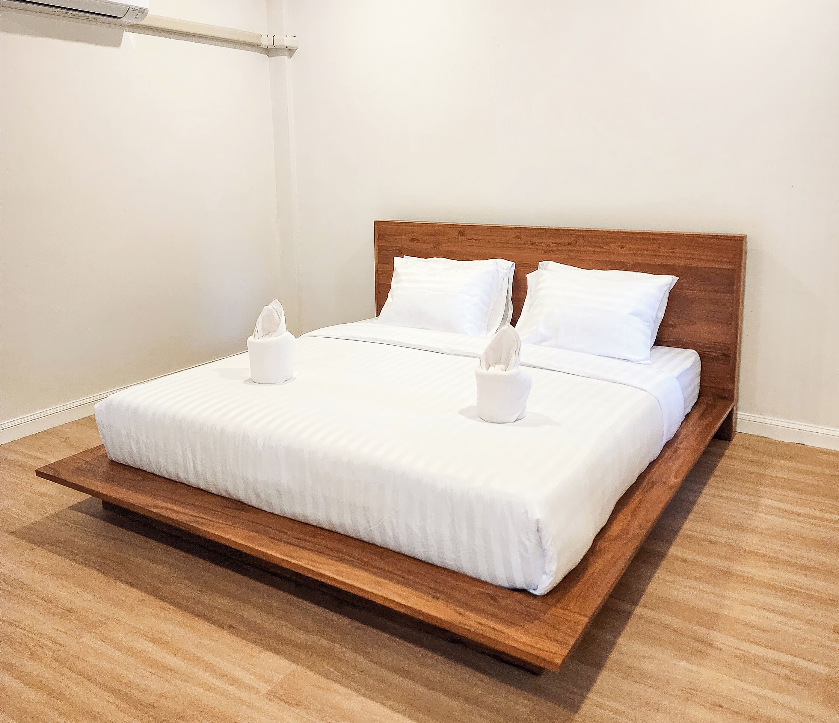 Un lit bien fait, avec du linge de lit blanc et deux oreillers, une tête de lit en bois et une table de chevet sur laquelle se trouve une boîte de mouchoirs.