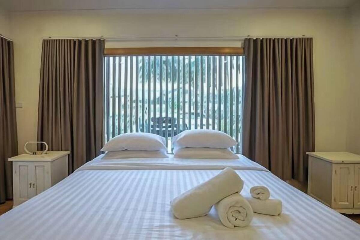 Habitación de hotel con una cama grande, dos mesitas de noche, una ventana con cortinas y vistas a zonas verdes.